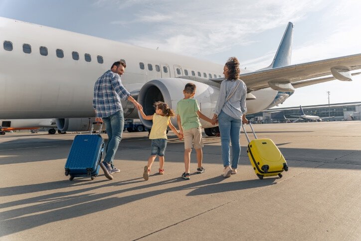 Smiling parents and kids walking with travel bags with a big plane in the background. Trip concept